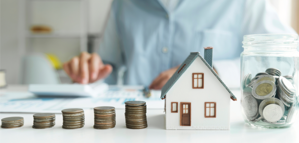 Coins stacked in ascending order, with a model house and jar of coins, financial planning concept.