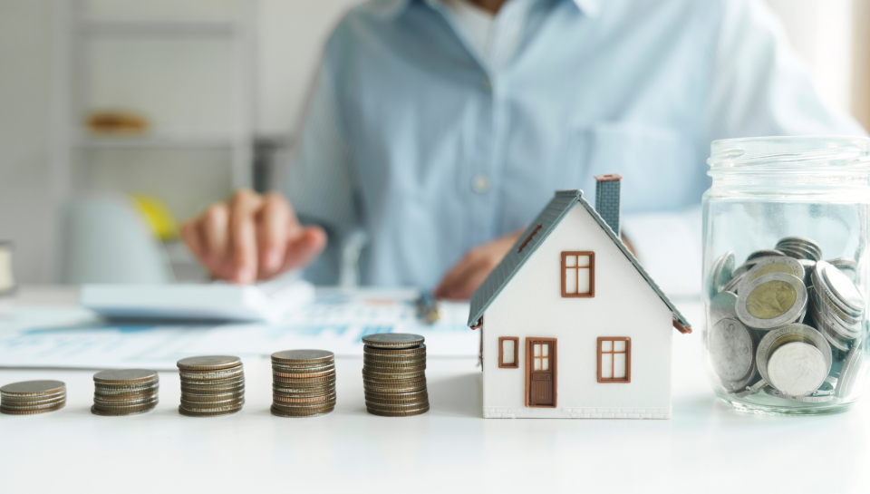 Coins stacked in ascending order, with a model house and jar of coins, financial planning concept.