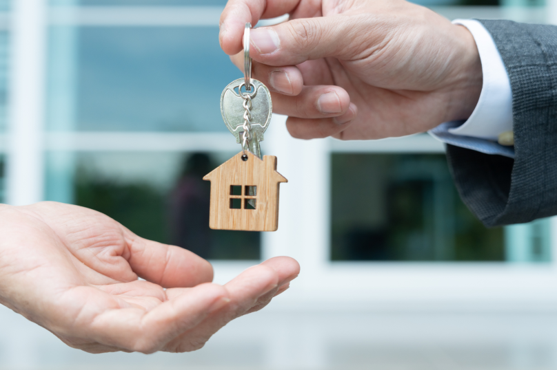 Home ownership transaction with key handover and house keychain in focus.