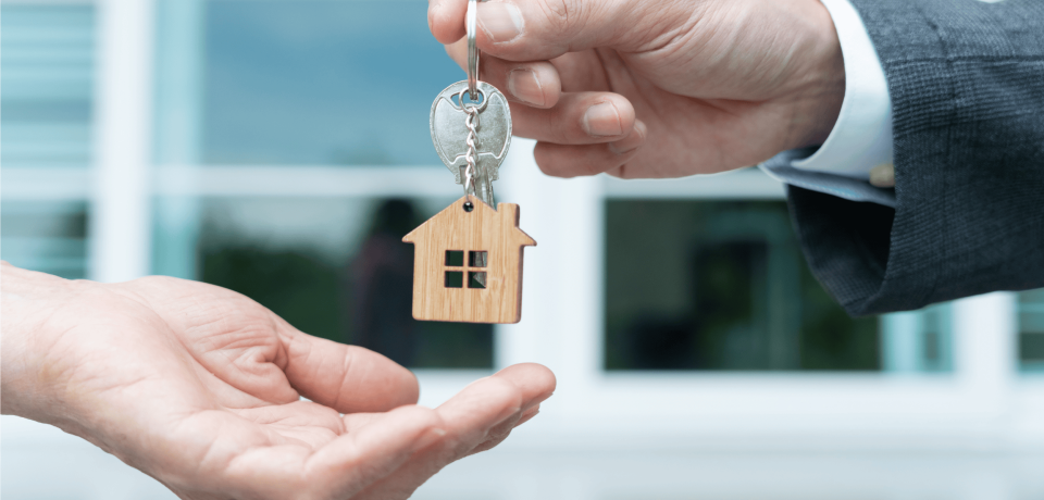 Home ownership transaction with key handover and house keychain in focus.