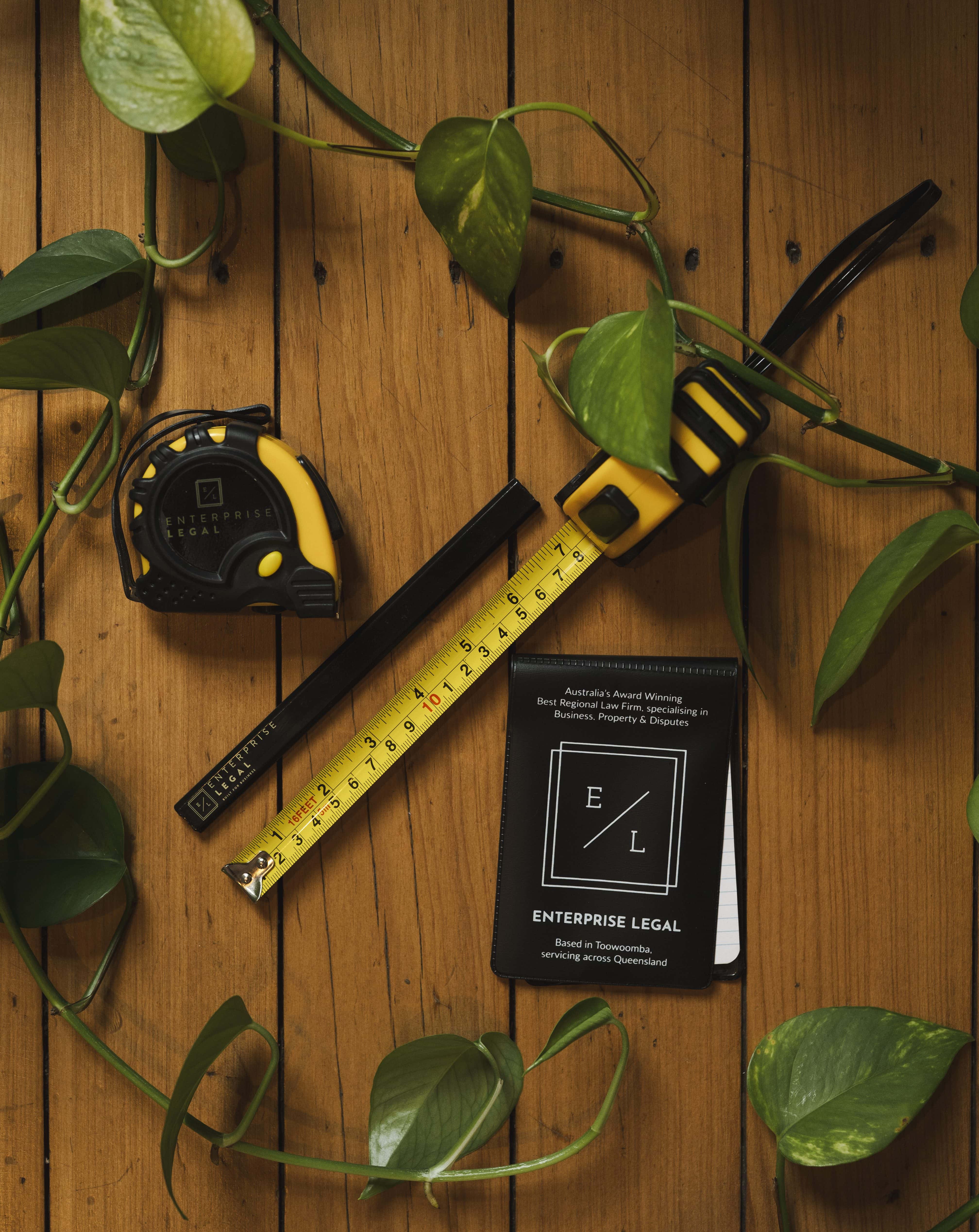 Measuring tape with enterprise legal branding and green ivy on wooden surface.