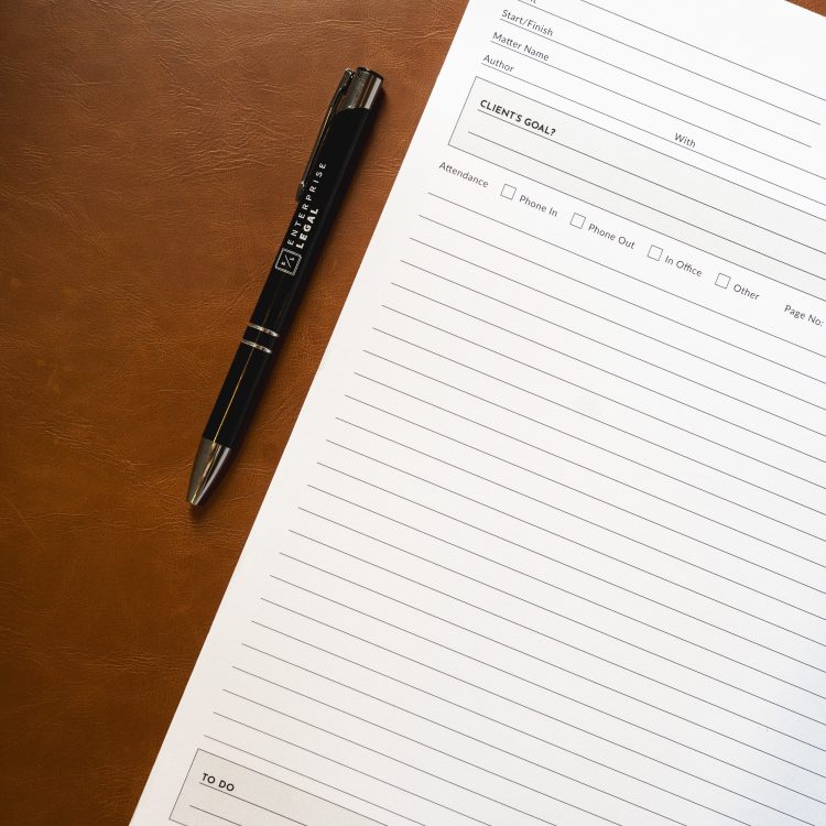 Legal file note paper with enterprise legal branded pen on brown leather desk.