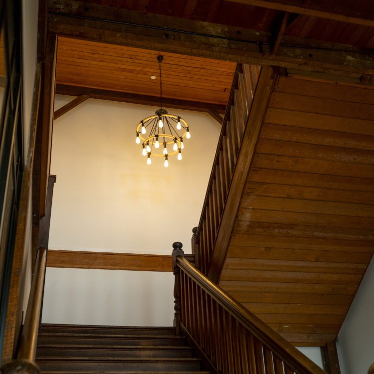 Staircase with wooden banisters and chandelier in a heritage-style building.