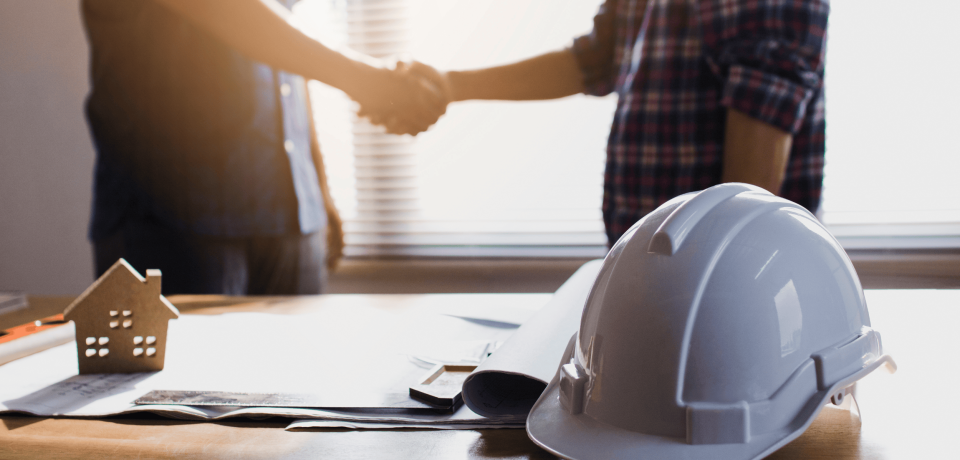 White safety helmets and a small paper house model on a desk.