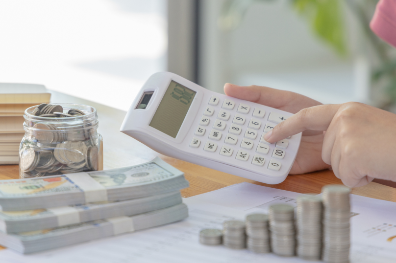 Coins in jar, calculator, and money stack on table representing financial planning, property, and legal services.