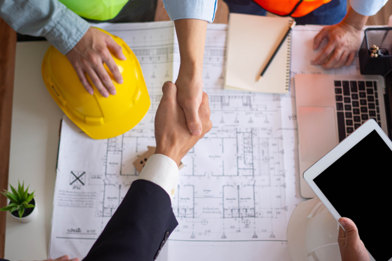 Construction project handshake at blueprints with safety helmet, law firm for property, construction law Queensland.