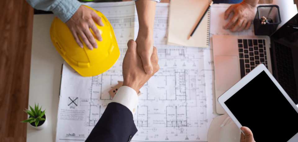 Construction project handshake at blueprints with safety helmet, law firm for property, construction law Queensland.